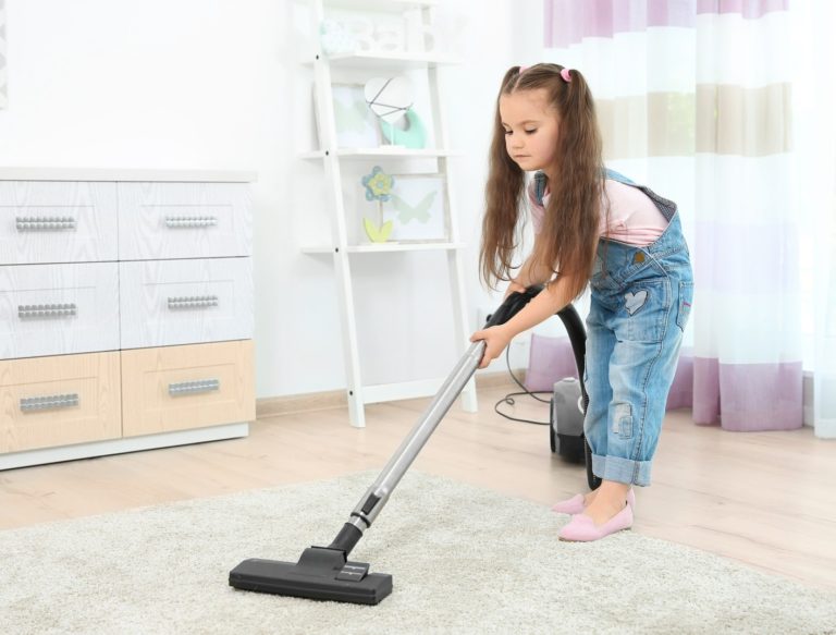 Cute little girl using vacuum cleaner in room